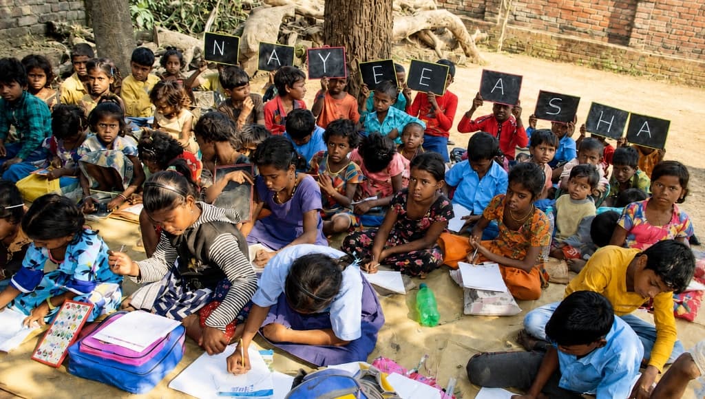 Children participating in a Nayee Asha outdoor learning activity, with students holding slates spelling the organisation's name.